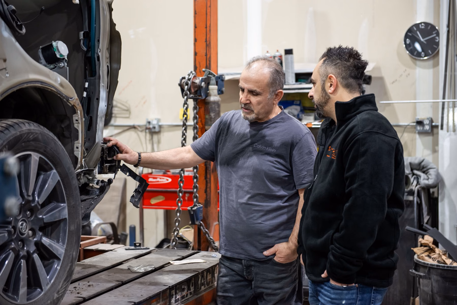 A senior collision technician walking a colleague through a repair on the frame rack.